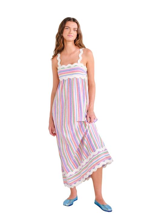 Woman wearing a colorful striped dress standing against a white background with a plant to her right.