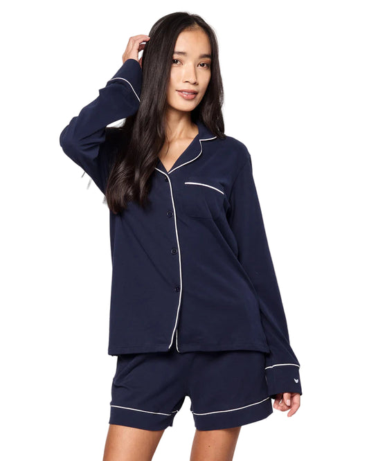 Woman wearing navy blue pajamas with white piping on a beige background