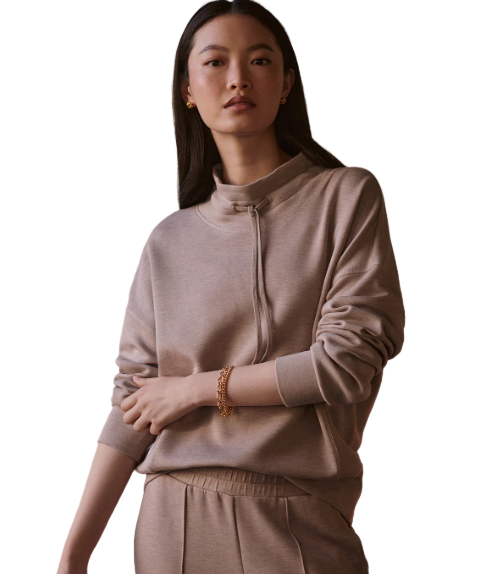 Woman wearing a beige hoodie and pants against a plain wall.