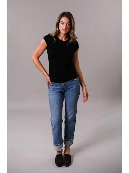 Woman wearing a black top and blue jeans against a gray background