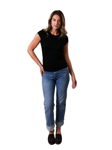 Woman wearing a black top and blue jeans against a gray background