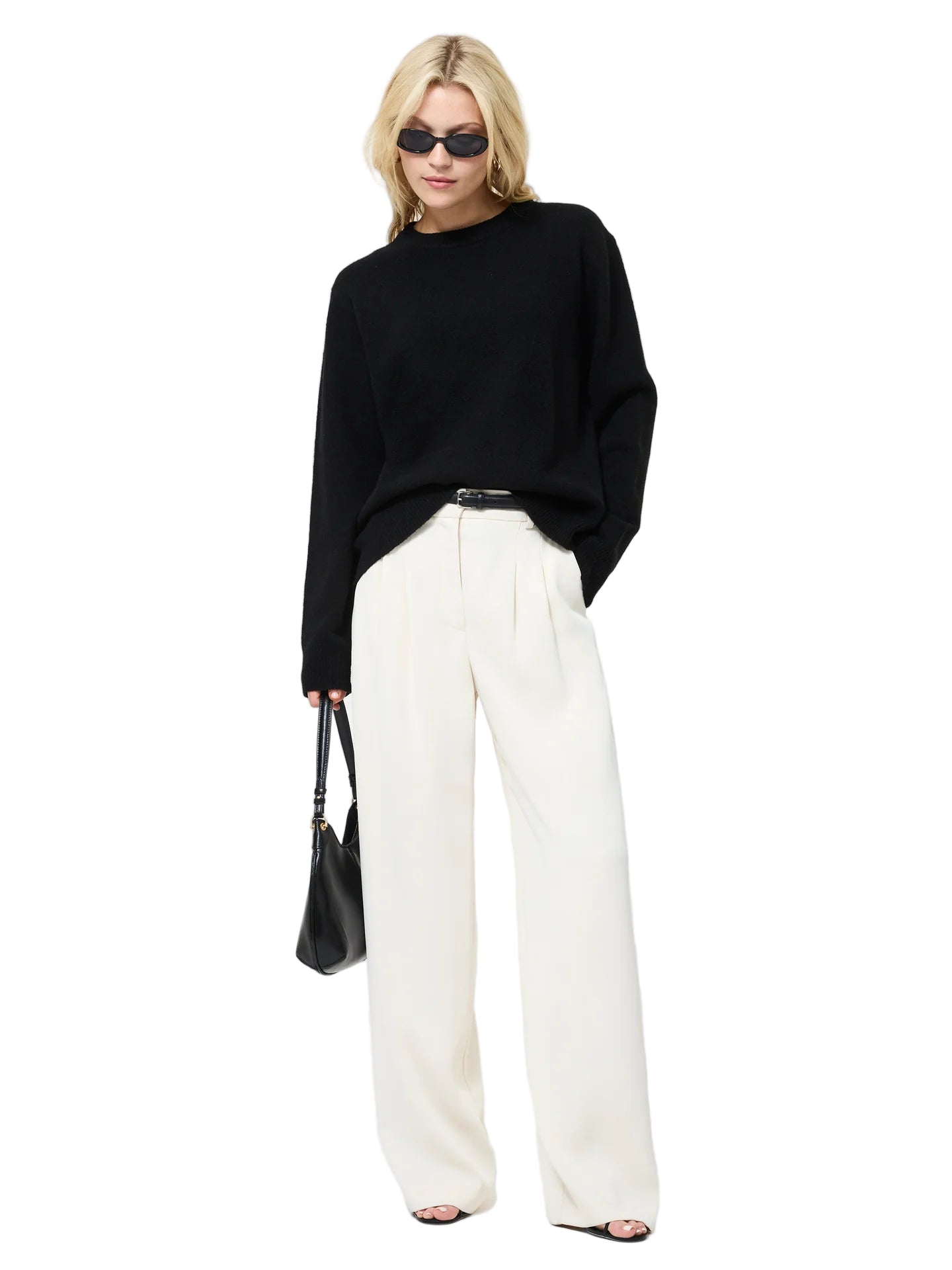 Person wearing a black sweater and white pants with a black handbag on a white background