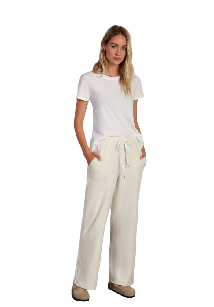 Woman wearing a white t-shirt and cream-colored pants against a plain background