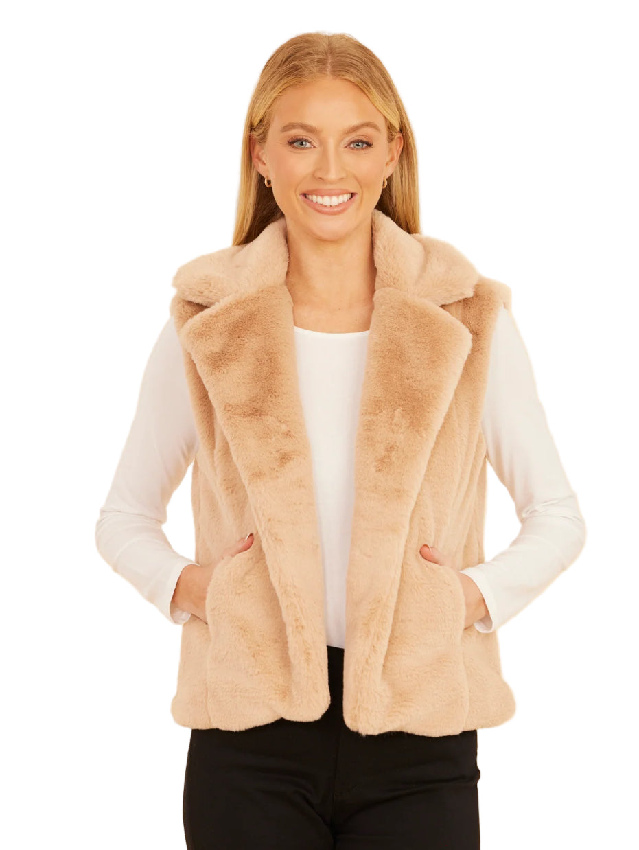 Woman wearing a beige faux fur vest against a beige background