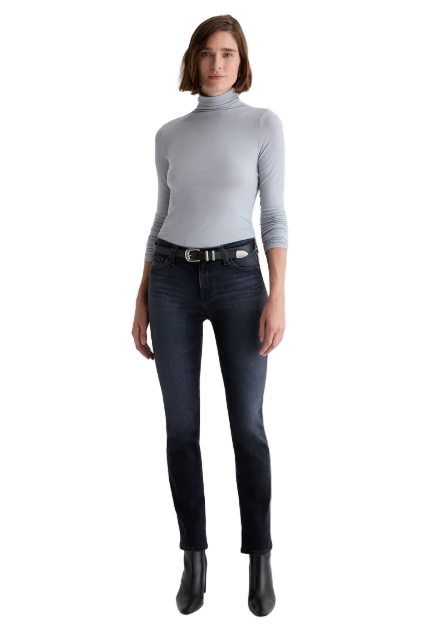 Woman wearing a gray turtleneck and dark jeans on a white background